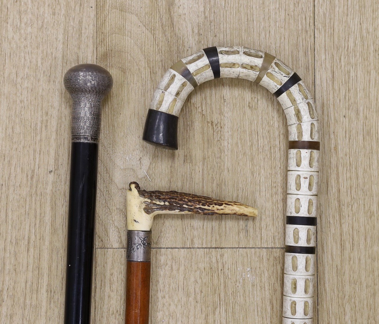 A silver mounted ebony walking cane, a shark vertebrae walking stick and a stag antler mounted malacca riding crop